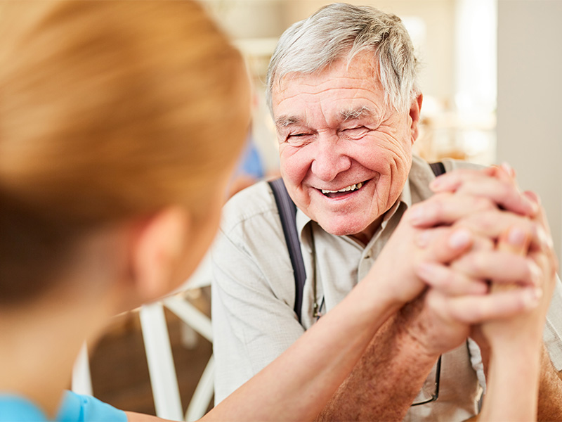 Ein älterer Mann lächelt hoffnungsvoll, während er liebevolle Unterstützung erhält, die ihm Zuversicht und Lebensfreude schenkt.