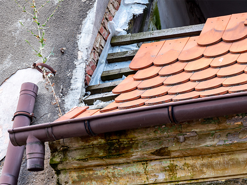 Dach eines Hauses nach einem Sturmschaden, Ziegel fehlen, sichtbare Decke und Abdeckung für temporären Schutz.