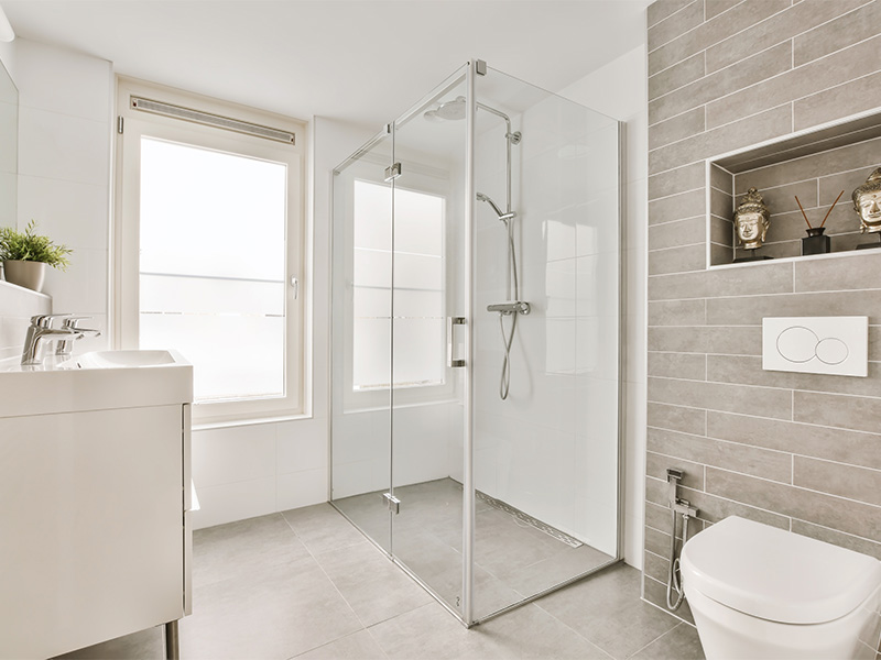 Kompaktes Badezimmer mit Eck-Glasdusche, Toilette und Waschbecken, hell gefliest und modern gestaltet.