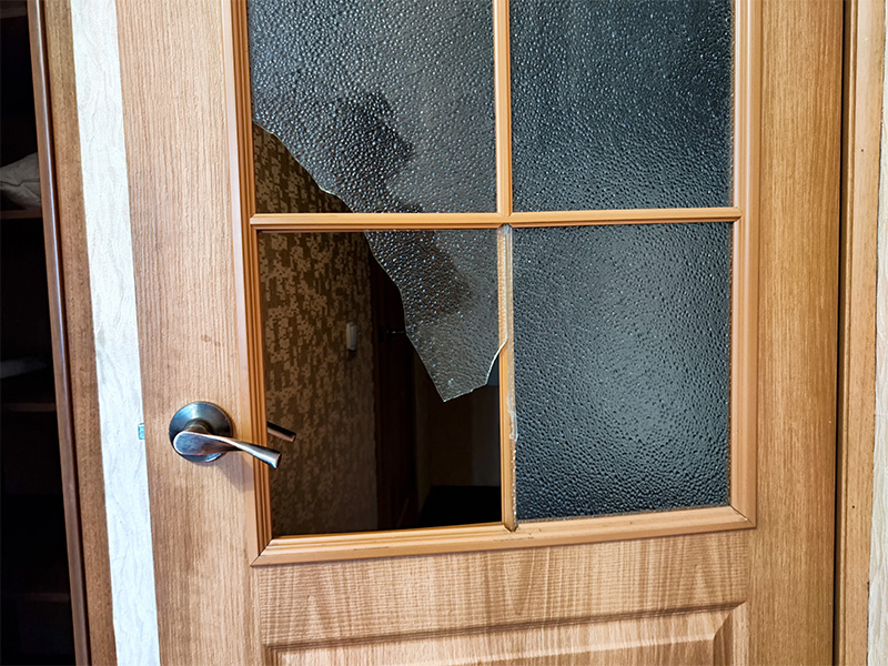 Zerbrochenes Glaspanel in einer Holztür mit sichtbaren Rissen und abgebrochenen Glasstücken.