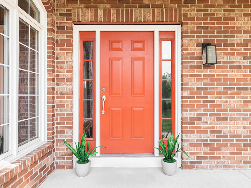 Rote Haustür mit Pflanzen und roten Backsteinen, umgeben von Fenstern – Symbol für stilvolle Haustüren in Meschede.