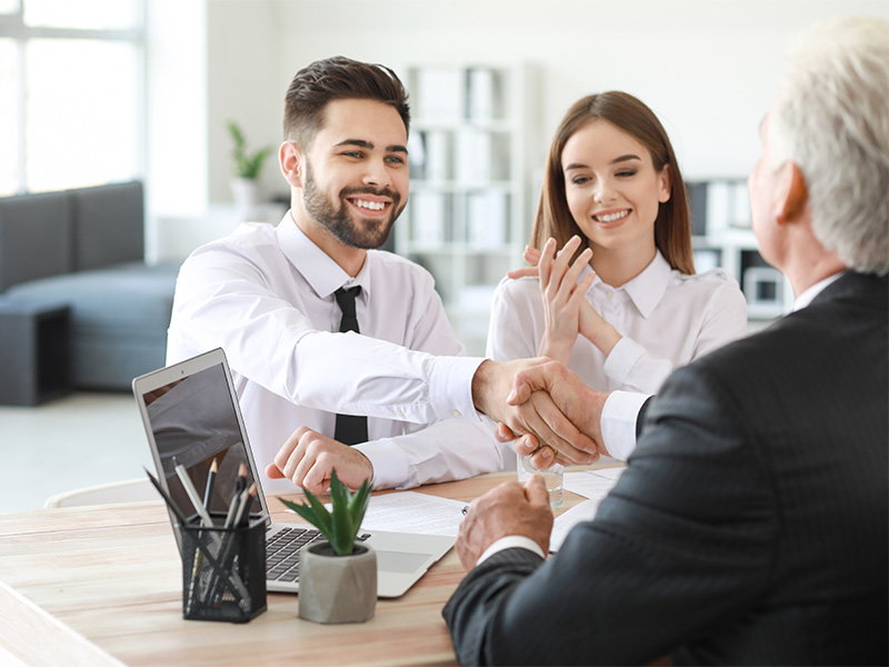 Zwei Personen schütteln Hände mit einem Notar bei der Beurkundung eines Kaufvertrags in Menden.