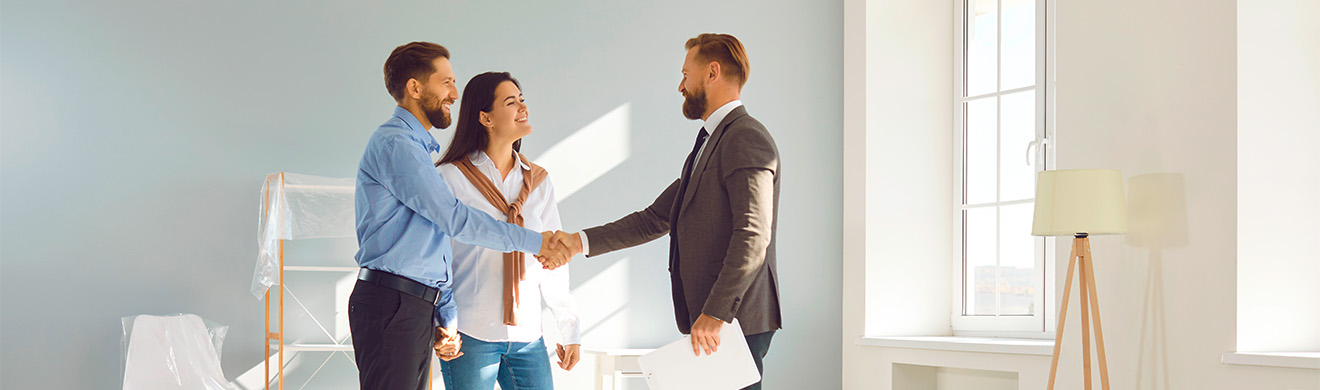 Junges Paar schließt einen Deal für den Kauf einer Wohnung und schüttelt einem Hausverwalter die Hand in Winterberg.