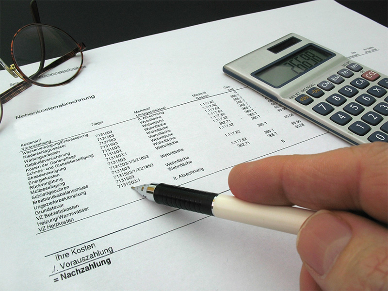 Hand zeigt auf Nebenkostenabrechnung mit Zahlen und Rechnungen – Symbol für Transparenz und Genauigkeit bei der Abrechnung.