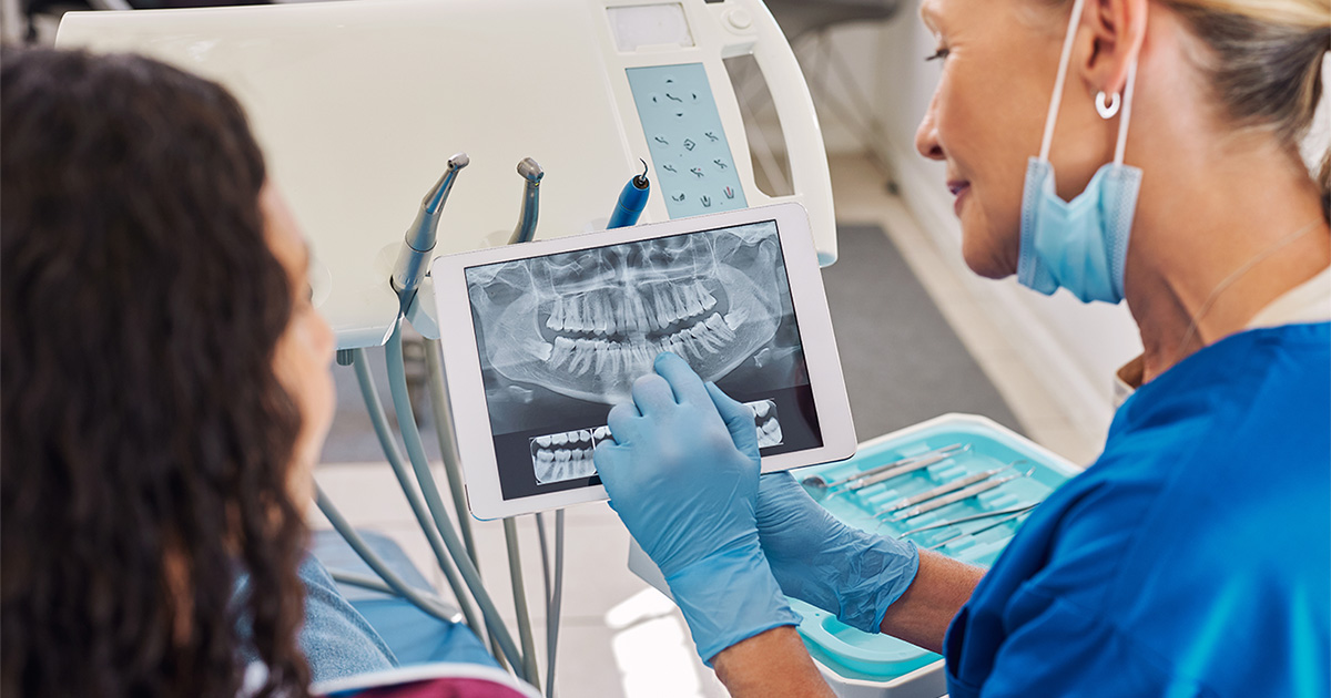 Kieferorthopädin zeigt Patientin digitale Röntgenaufnahme des Kiefers auf Tablet zur kieferorthopädischen Diagnostik und Behandlungsplanung in moderner Praxis