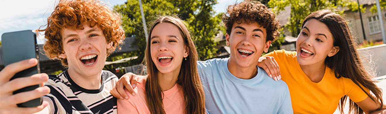 Fröhliche lächelnde Gruppe von Teenagern, die gemeinsam im Skatepark sitzen, Selfie machen und Freizeit genießen und Spaß haben