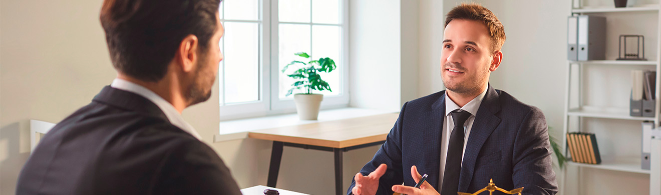 Anwalt im Anzug berät einen Mandanten am Schreibtisch, erklärt rechtliche Fragen und gibt professionelle Ratschläge zu Arbeitsrecht.