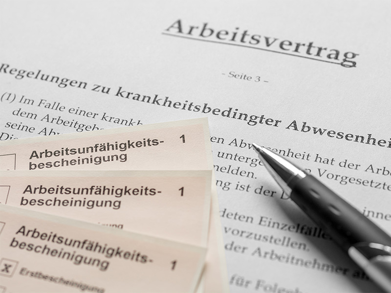 Arbeitsvertrag und Arbeitsunfähigkeitsbescheinigungen auf einem Schreibtisch, die Regelungen zum Kündigungsschutz dokumentieren