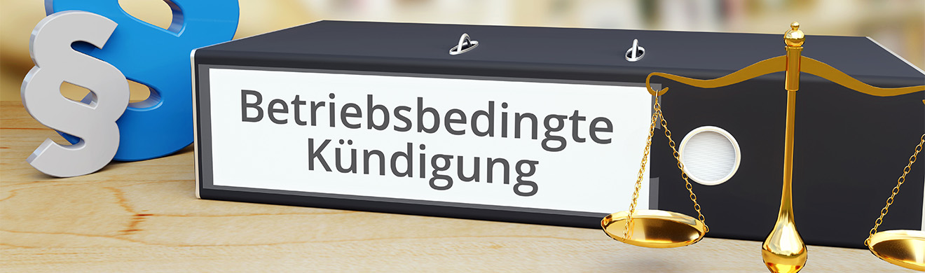 Aktenordner mit Aufschrift „Betriebsbedingte Kündigung“ und Paragrafen-Symbol auf Schreibtisch, symbolisiert rechtliche Beratung in Menden.