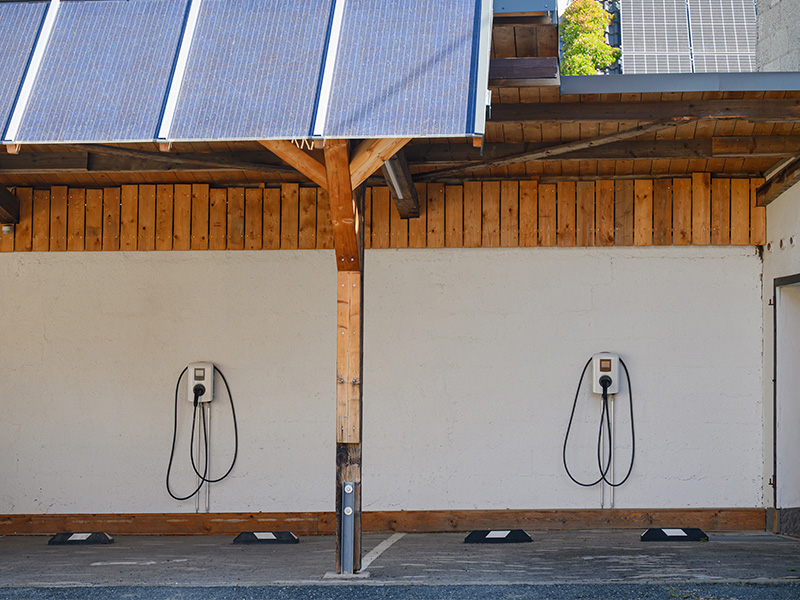 Zwei Wallboxen zur Elektroauto-Ladung an einem Carport mit Solarpanelen auf dem Dach.